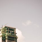 Edifício alto em construção, com estrutura aparente, contra o céu claro em uma área urbana.