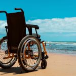 Cadeira de rodas posicionada sobre a areia diante do mar em um dia ensolarado