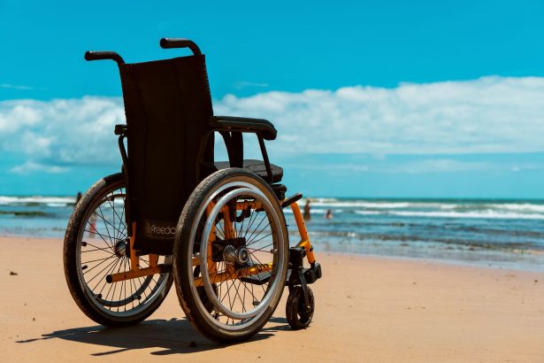 Cadeira de rodas posicionada sobre a areia diante do mar em um dia ensolarado